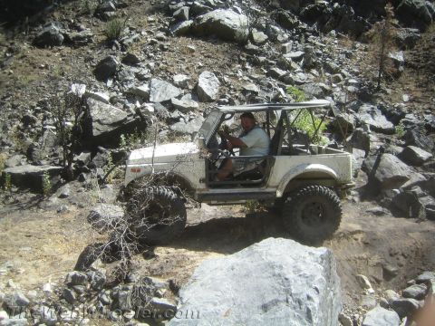1987 Suzuki Samurai - A white 1987 Suzuki Samurai navigates a challenging rocky terrain on a sunny day.