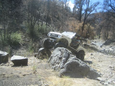 1987 Suzuki Samurai - A white 1987 Suzuki Samurai navigates a rocky trail, demonstrating its off-road capabilities.