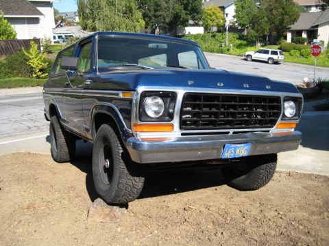 Blue 1978 Ford Bronco parked on dirt with a rock under the front tire