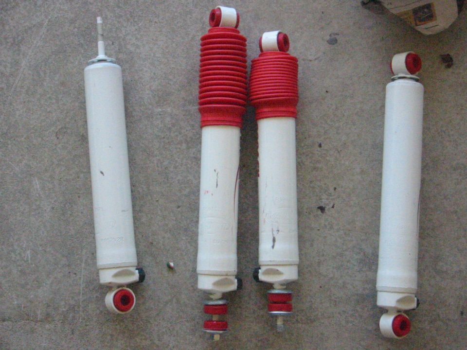 Four white and red shock absorbers laid out on a concrete surface
