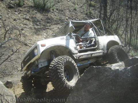 1987 Suzuki Samurai - A driver navigates a white Suzuki Samurai over large rocks on a steep, rocky trail.