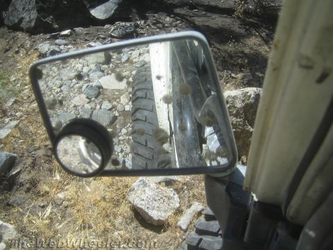 1987 Suzuki Samurai - A vehicle's tire and side mirror are visible on a rocky, off-road path.