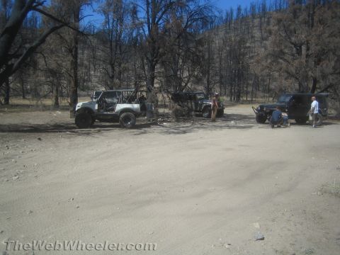 1987 Suzuki Samurai - Several off-road vehicles are parked on a dirt path amidst a landscape of burnt trees.