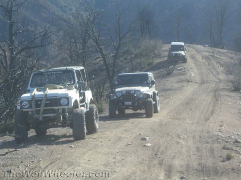 1987 Suzuki Samurai - A convoy of off-road vehicles, including a Suzuki Samurai and Jeeps, navigates a dusty trail on a hillside.