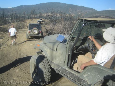 1987 Suzuki Samurai - Several Jeeps drive on a dusty, off-road trail through a landscape with burnt trees.