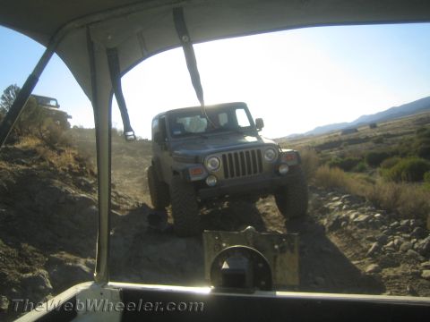 1987 Suzuki Samurai - Two Jeeps navigate a challenging off-road trail under a clear sky.