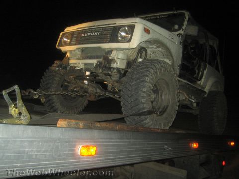 1987 Suzuki Samurai - A white 1987 Suzuki Samurai is loaded onto a flatbed truck at night, showing its modified suspension and large off-road tires.