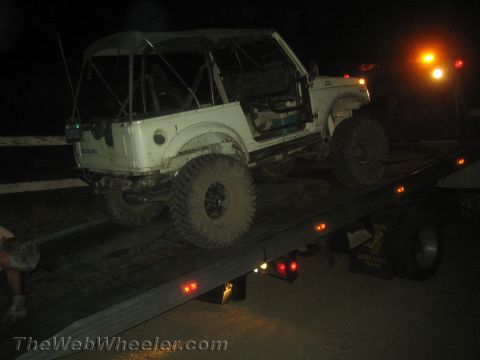 1987 Suzuki Samurai - A white 1987 Suzuki Samurai is loaded onto a tow truck at night, with the "SUZUKI" badge clearly visible on the rear.