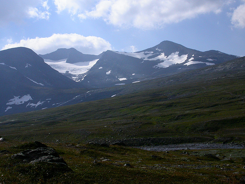 Mountain range with snow-capped peaks and a glacier under a cloudy sky
