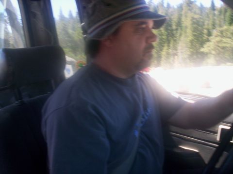 1989 Ford Bronco - Driver in a hat behind the wheel of a vehicle with trees in the background.