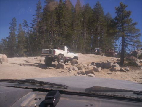 1989 Ford Bronco - Several off-road vehicles are seen traversing a challenging rocky path under a clear blue sky.