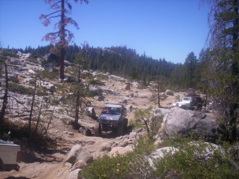 1989 Ford Bronco - Multiple off-road vehicles traverse a challenging, rocky terrain under a clear blue sky.