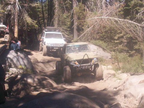 1989 Ford Bronco - A convoy of off-road vehicles navigates a challenging rocky path through a forest.