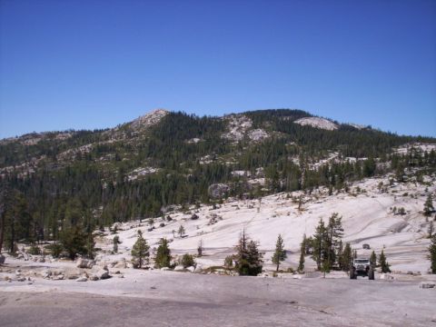 1989 Ford Bronco - An off-road vehicle is parked in a scenic mountain area with sparse trees and rocky terrain.
