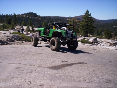 1989 Ford Bronco - A heavily modified off-road vehicle is parked on a rocky terrain under a clear blue sky.