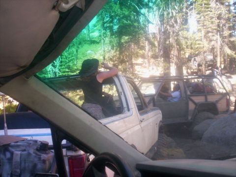 1989 Ford Bronco - A group of off-road vehicles are parked in a wooded area, with one person leaning out of the window of a white truck.