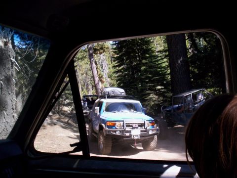 1989 Ford Bronco - Two off-road vehicles drive on a dusty forest road.