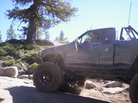 1989 Ford Bronco - Modified pickup truck with large tires navigating a challenging off-road trail.
