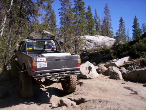 1989 Ford Bronco - A lifted pickup truck navigates a rocky off-road trail under a clear blue sky.