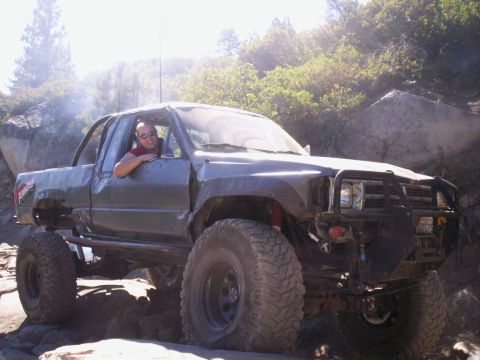 1989 Ford Bronco - This heavily modified pickup truck is shown off-roading on a sunny day, with a driver visible behind the wheel.