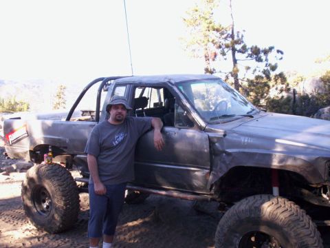 1989 Ford Bronco - A man poses next to a heavily modified pickup truck with oversized tires and a custom roll cage, suggesting off-road use.