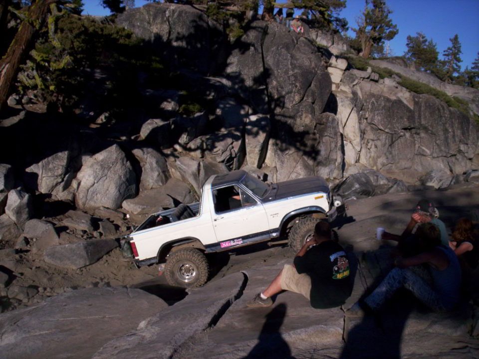 White Ford Bronco with black hood navigating a rocky trail, people watching