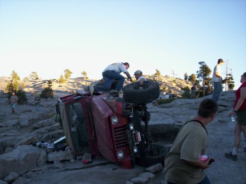 1989 Ford Bronco - A red 1989 Ford Bronco has rolled onto its side in a rocky, off-road environment.