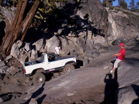 1989 Ford Bronco - A modified SUV navigates a challenging rocky trail under a clear blue sky.