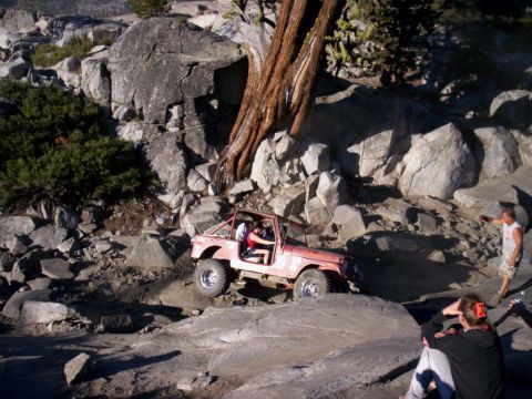 1989 Ford Bronco - A red off-road vehicle maneuvers through a challenging rocky landscape with onlookers present.