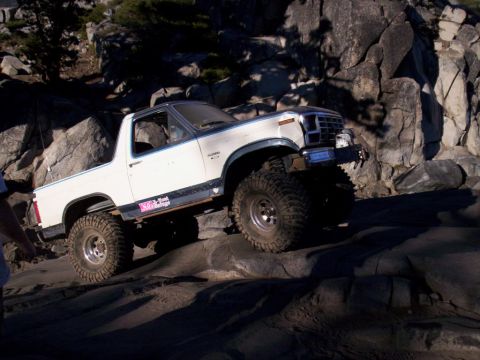 1989 Ford Bronco - This lifted 1980s Ford Bronco is shown off-roading over large rocks, with a pink sticker on its side reading 'NOX-Raptor Garage'.