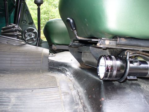 1978 Ford Bronco - Interior floor detail beside a green vinyl bucket seat, showing a black Maglite-style flashlight clipped into a mount on the transmission t…