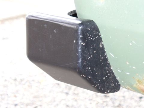 1978 Ford Bronco - Close-up of a rear bumper corner a black rubber protector with white flecks, attached to a light green vehicle body.