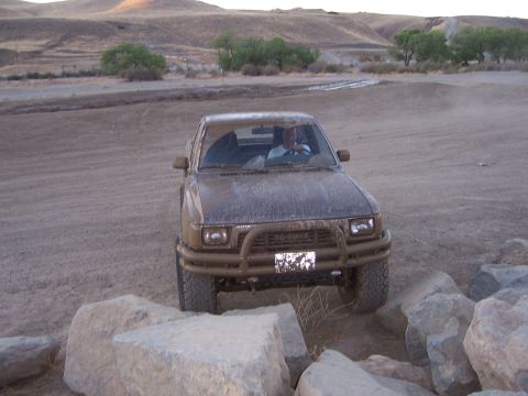 1991 Ford Bronco - A driver navigates a muddy, rocky terrain in a brown SUV.