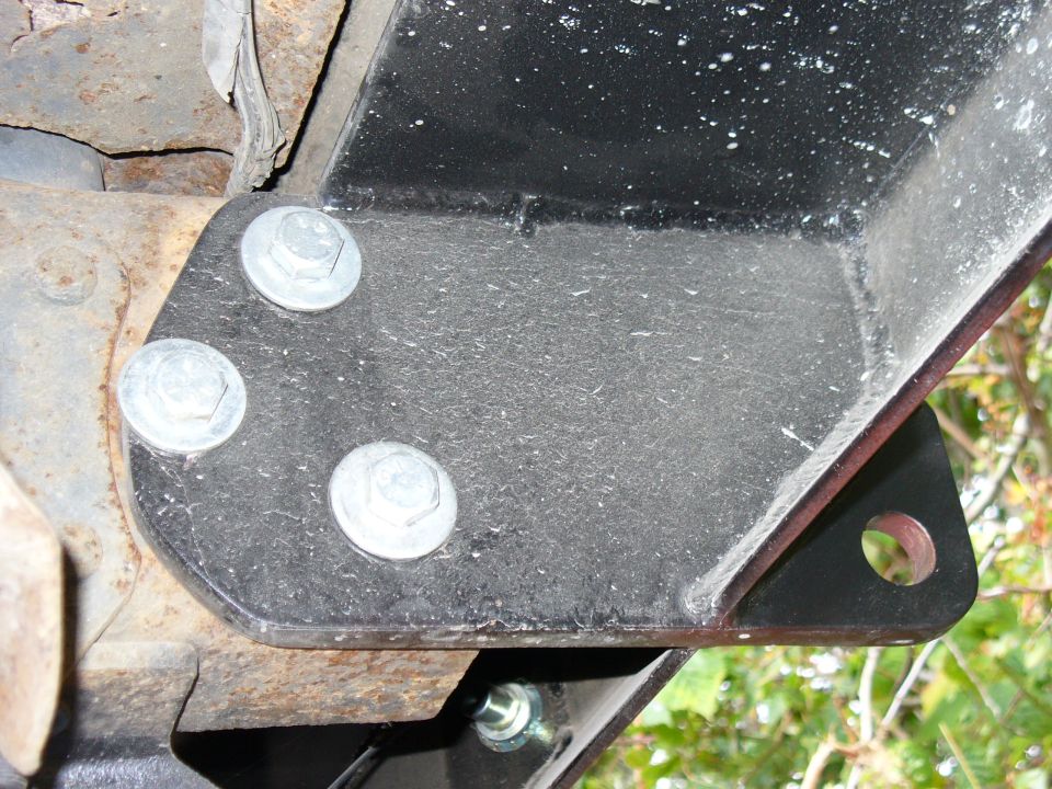 Close-up of a black metal bracket bolted to a rusty vehicle frame with three large bolts