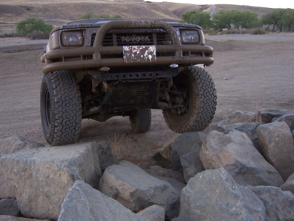 Mud-covered Toyota SUV with a bull bar and off-road tires on rocks