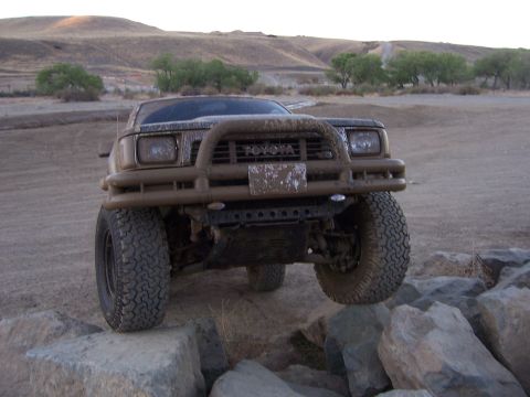 1991 Ford Bronco - Muddy Toyota pickup truck navigates rocky terrain with a bull bar installed.