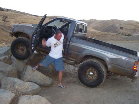 1991 Ford Bronco - A man exits a gray pickup truck as it maneuvers over rocks.