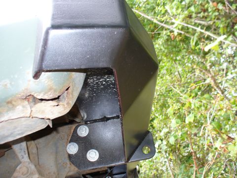 1978 Ford Bronco - Close-up of a black bumper bracket bolted to a heavily rusted quarter panel, with foliage in the background.