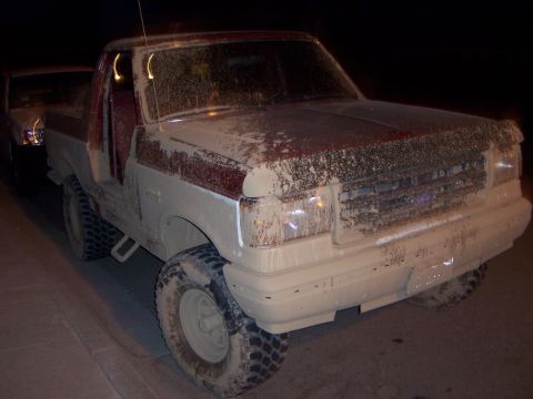 1991 Ford Bronco - A muddy pickup truck is parked next to another vehicle at night.