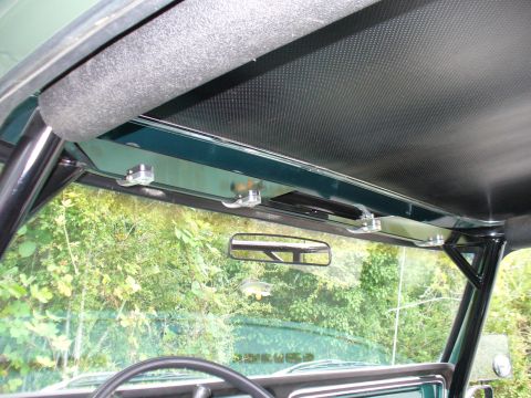 1978 Ford Bronco - The interior of a vehicle shows a roll cage and a rear-view mirror reflecting trees outside.