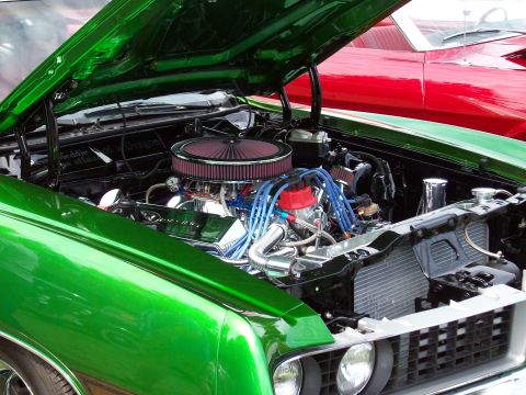 1997 Ford Mustang - The engine bay of a shiny green classic car is open, revealing a detailed engine and a red car in the background.