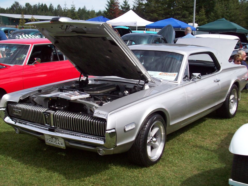 Silver 1969 Mercury Cougar with hood and trunk open, parked on grass. Red car visible to the left