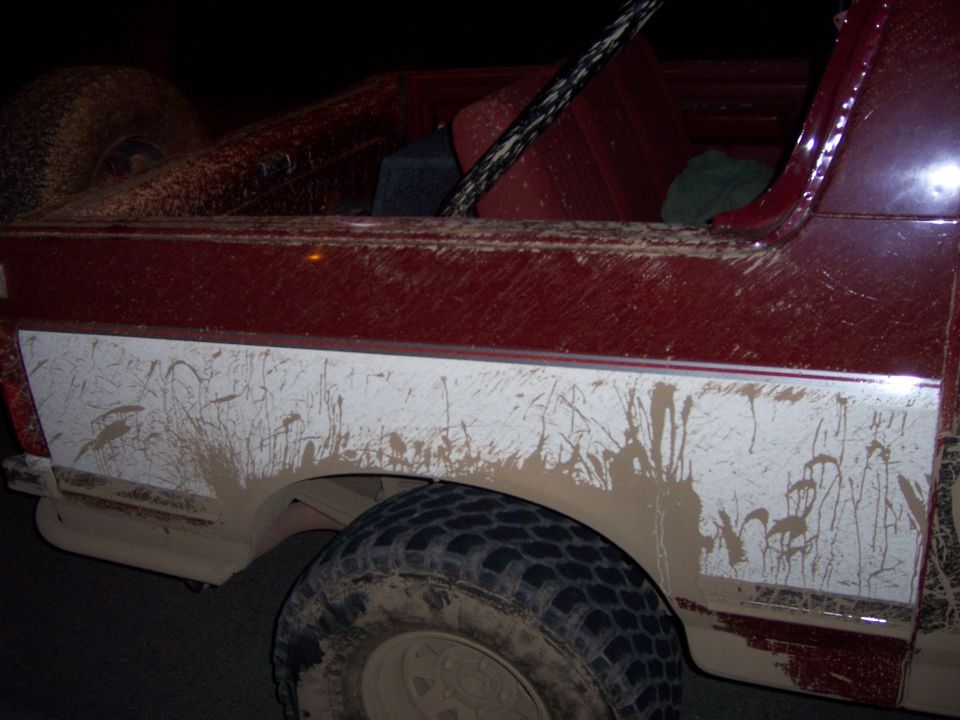Mud covers the side of a red SUV, with a spare tire visible in the back