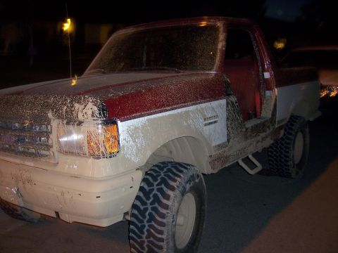 1991 Ford Bronco - A muddy Ford Bronco is parked at night with its driver's door ajar.