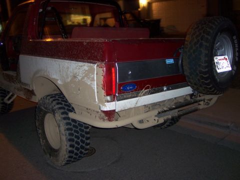 1991 Ford Bronco - Mud-covered 1991 Ford Bronco rear view, a spare tire and roll bar.
