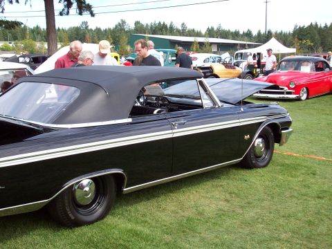 1997 Ford Mustang - Black convertible with white side stripe and chrome hubcaps at a car show. Another car is visible in the background.