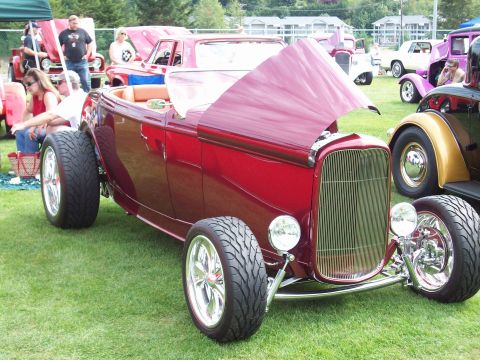 1997 Ford Mustang - A shiny red hot rod is displayed at an outdoor car show with several other vehicles and attendees present.