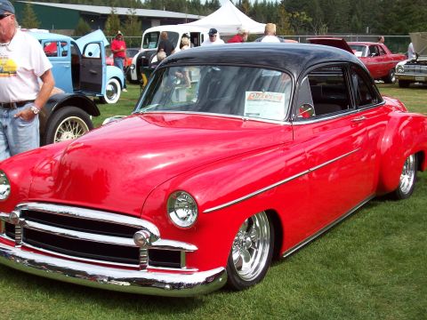 1997 Ford Mustang - A classic red coupe with a black roof is displayed at an outdoor car show with other vehicles in the background.