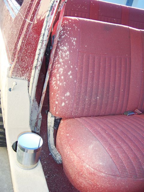 1991 Ford Bronco - The interior of a vehicle shows red seats covered in white dust, with a tin can visible on the floor.