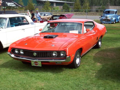 1997 Ford Mustang - An orange 1970 Ford Torino GT is parked on grass next to other vehicles.